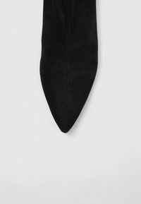 Chaussure noire en velours ras à bout pointu avec des coutures verticales et une texture lisse, présentant un design élégant et une silhouette minimaliste.