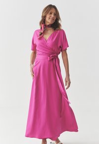 Pink wrap dress with short sleeves, a tied belt at the waist, and a flowing skirt. Includes a multicolored scarf around the neck. Smooth texture.