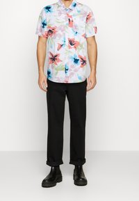 Lyhythihainen nappikauluspaita kevyestä materiaalista, jossa on monivärinen kukkakuosi. Mustat housut ja massiiviset mustat saappaat tekevät asusta täydellisen.