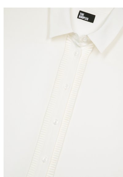 Weißes Hemd aus weichem Material mit Kragen, gerippter Knopfleiste und transparenten Knöpfen. Etikett trägt "The Kooples."