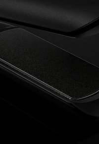 Une surface noire texturée présente un bord incurvé brillant avec un effet de brillance subtil. La zone lisse et plate contraste avec la texture rugueuse.