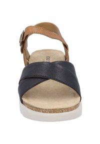 Black leather sandal with crisscross design, tan leather strap, and adjustable buckle. Light-colored textured footbed and white sole.