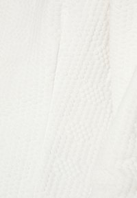 Toalha branca com textura, apresentando um padrão de pontos elevados e uma superfície lisa. O tecido parece suave e absorvente.