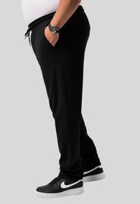 Pantalones de chándal negros con cintura ajustable, bolsillos laterales y un corte holgado, combinados con zapatillas Nike negras que presentan un logo blanco.