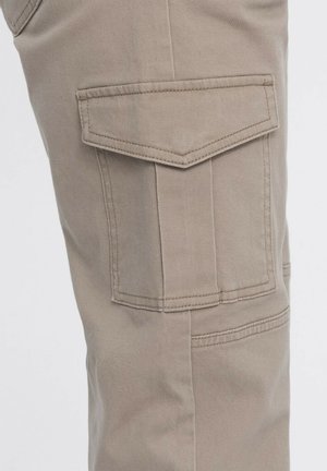 Pantalones cargo beige con un tejido texturizado, que presentan un gran bolsillo en forma de triángulo en el lateral y detalles de costura doble.