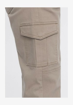 Pantalones cargo beige con un tejido texturizado, que presentan un gran bolsillo en forma de triángulo en el lateral y detalles de costura doble.