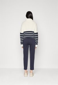 Vit och marinrandig stickad tröja med hög krage, kombinerad med marinblå smalbeniga byxor och ljusa beige skor. Slät struktur, avslappnad design.