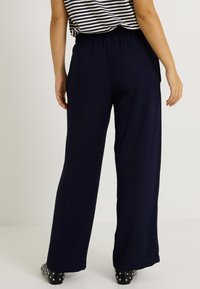 Pantalons larges bleu marine avec une taille élastique, en tissu texturé et avec une coupe décontractée, associés à un haut rayé et des chaussures noires à clous.