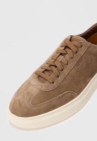 Brown suede sneaker with matching laces, white sole, and "BOSS" embossed on the side, shown against a white background.