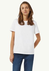 Witte katoenen T-shirt met korte mouwen, ronde halslijn en een losse pasvorm. Draagt bij blauwe denim jeans. Eenvoudig ontwerp, geen patronen of accenten.