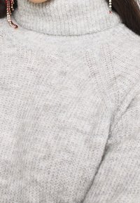 Light gray turtleneck sweater made of soft, textured knit material with subtle pattern details. Close-up view highlights the fabric's quality.