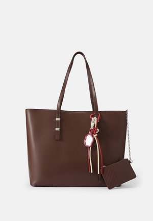 Bolsa tote de couro castanho com duas alças, detalhes em metal prateado, franjas decorativas e uma pequena carteira com fecho a zíper combinando presa.