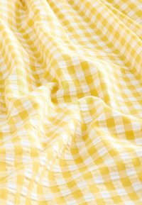 Gult ginghamtyg med ett rutmönster av v�äxelvis gula och vita rutor, mjuk textur och lätt drapering.