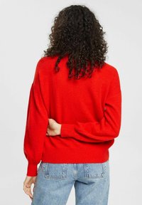 Roter, übergroßer Strickpullover mit langen, voluminösen Ärmeln und gerippten Bündchen. Weiche Textur, schlichtes Design, kombiniert mit hoch taillierten Jeans.