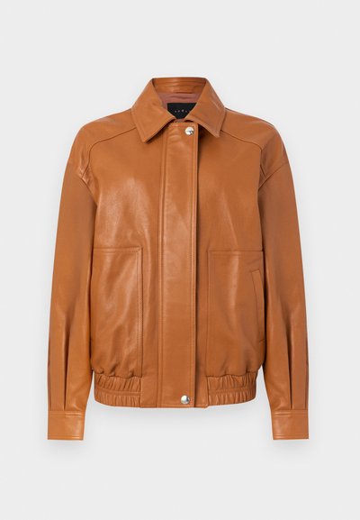 Καφέ δερμάτινο μπουφάν με μπροστινά κουμπιά με παττάκι, ελαστική μέση, δύο μεγάλες μπροστινές τσέπες και μυτερό γιακά σε λευκό φόντο.