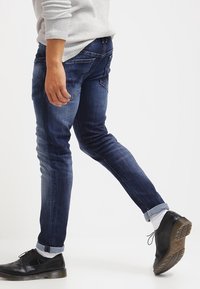 Slim-fit jeans i mörkblå denim, med lätt blekning, dragkedja i gylfen och fem fickor. Kombinerat med svarta skor och uppvikta ben.