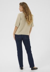 Un pull en tricot beige à manches courtes avec une finition texturée, associé à un jean droit bleu foncé et des ballerines noires, vu de l'arrière.