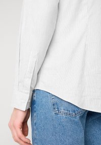Langärmliges Hemd mit weißen und grauen Streifen und knöpfbaren Manschetten, präsentiert zusammen mit hellblauem Denim. Verfügt über einen abgerundeten Saum und ein strukturiertes Gewebe.