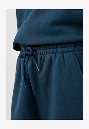 Pantalon de survêtement bleu foncé avec taille élastique et cordon noué, haut en tissu bleu foncé assorti partiellement visible.