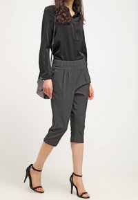 Musta satiinipaita pitkillä hihoilla, yhdistettynä korkeavyötäröisiin harmaisiin mittatilaustyönä tehtyihin capri-housuihin ja mustiin remmikorkokenkiin. Mukana pieni olkalaukku.