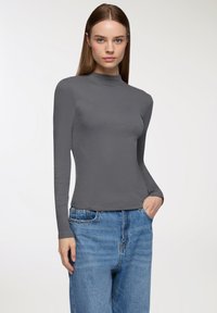 Szara, długoramienna koszulka z golfem o prążkowanej fakturze, dopasowanym kroju i okrągłym dekolcie. Połączona z niebieskimi dżinsami o wysokim stanie.