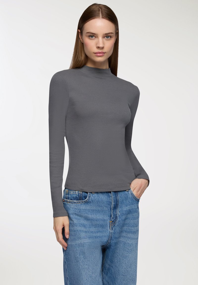 Szara, długoramienna koszulka z golfem o prążkowanej fakturze, dopasowanym kroju i okrągłym dekolcie. Połączona z niebieskimi dżinsami o wysokim stanie.