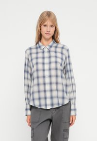 Camisa às riscas em azul claro e branco, com botão na frente, mangas longas e bainha arredondada. Feita de tecido leve e macio.