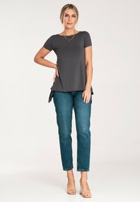 Szary top z krótkim rękawem i zaokrąglonym dołem, w połączeniu z niebieskimi jeansami o wysokim stanie. Modelka nosi przezroczyste obcasy i delikatny złoty naszyjnik.