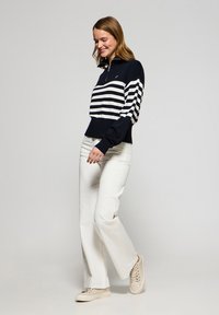 Marinblå och vit randig tröja med zipkrage; mjukt stickat tyg, långa ärmar och ribbad nederkant. Matchas med vita vida byxor och ljusa sneakers.