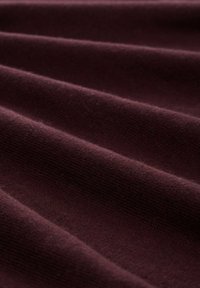 Bordeaux gekleed stof met diagonale plooien, die een zachte breipatroon laat zien. Het materiaal lijkt warm en iets harig.