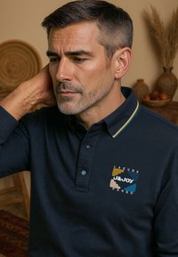 Marineblauwe polo met een textuurstof, gekenmerkt door een kraag met gele, groene en witte strepen. Inclusief een meerkleurig geborduurd logo.