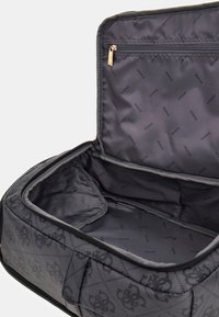 Borsa nera in materiale sintetico con texture trapuntata, zip dorata e interno grigio con motivo ripetuto "Guess". Ampio scomparto con tasca laterale.