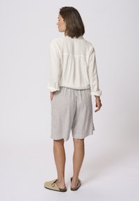 Cream linen blouse and striped shorts in muted tones, with a relaxed fit. The shorts have pockets and fall mid-thigh. Beige slip-on shoes.