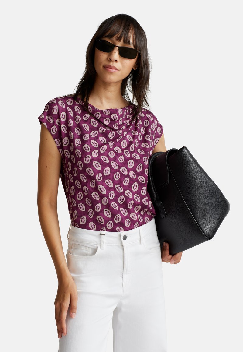 Haut à motifs violets avec des manches courtes, associé à un jean blanc et un sac à main noir texturé. Le tissu a une finition douce.