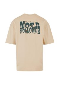 Beige cotton t-shirt featuring bold black text on the back, reading "NOT A FOLLOWER" with smaller text above and below. Classic crew neck design.