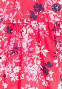 Tela floral con una base vibrante en color rosa, adornada con flores blancas, rosa claro y azul marino. El diseño incluye un detalle de cintura fruncida.