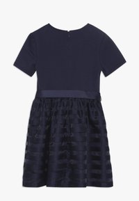 Vestito navy blue a maniche corte con parte superiore aderente, gonna a strisce orizzontali testurizzate e chiusura con zip sul retro.