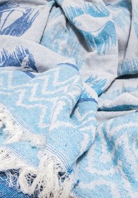 Blue and white woven fabric with zigzag and bird patterns, featuring fringed edges, laid out in soft folds.