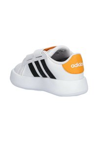 Sneaker bianco con strisce nere e accento arancione sul tallone. Presenta un materiale sintetico liscio e una cinghia con chiusura a strappo per una vestibilità sicura.