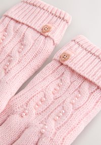 Strikkede lyserøde vanter med kabelmønster, små dekorative perler og en opsmøget kant med en hjerteformet knap som pynt.