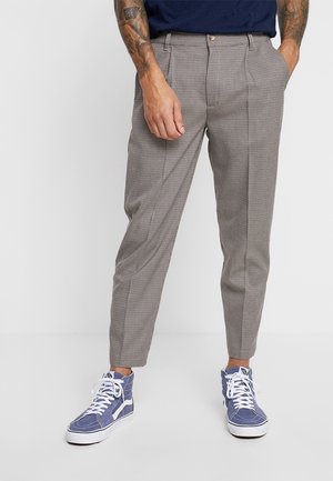 Grijze geblokte broek met een hoge taille, plooien aan de voorkant en een taps toelopende pasvorm, gecombineerd met blauwe hoge sneakers. Geschikt voor casual draagstijl.