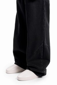 Svart oversized denim-bukse med oppbrettede kanter, kombinert med lyse, spisse sko med glatt tekstur og minimalistisk design.