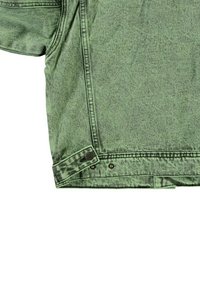 Vihreä denim-takki, jossa on rento istuvuus, napitus ja hienovarainen texture. Kangas on kuluneen näköinen, jossa on tummempia vivahteita helman kohdalla.