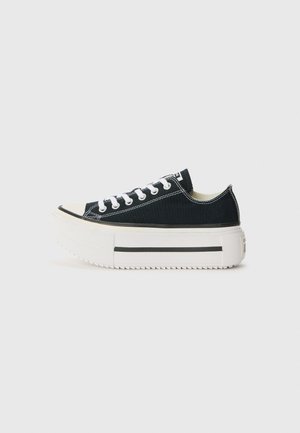 Zapatillas de lona negras con suela de goma blanca, que cuentan con una plataforma gruesa, cordones blancos y costuras en contraste a lo largo de las costuras.