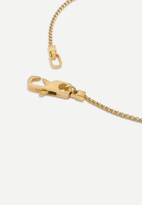 Collier chaîne doré avec un fermoir à homard. La chaîne présente un motif tressé et un logo de marque gravé sur le fermoir.