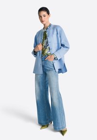 Svetlo modra volna jakna z okroglim izrezom, združena z živahno cvetlično bluzo in širokimi kavbojkami z razširjenimi nogami. Zelene čeveljčke s koničastim prstom.