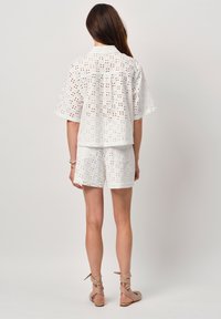 Witte katoen set met een T-shirt met korte mouwen en shorts met oogjes borduursel. Ontworpen met een ontspannen pasvorm en strakke lijnen.
