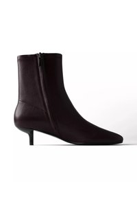 Bottine noire en cuir avec bout pointu, fermeture éclair latérale et petit talon kitten sur fond blanc.