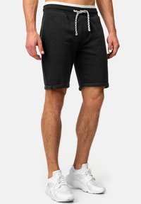 Pantalones cortos de mezcla de algodón gris con puños enrollados, cintura elástica y cordón blanco. Combinados con zapatos deportivos blancos.