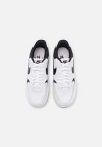 White Nike sneakers with black accents, featuring a smooth leather upper, perforated toe box, flat white laces, and a black inner lining.
